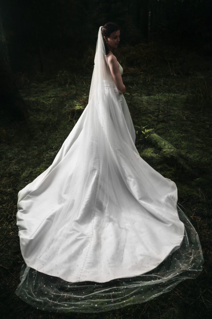 Bride seen from behind in dark woodland, her gown and veil spread across the ground