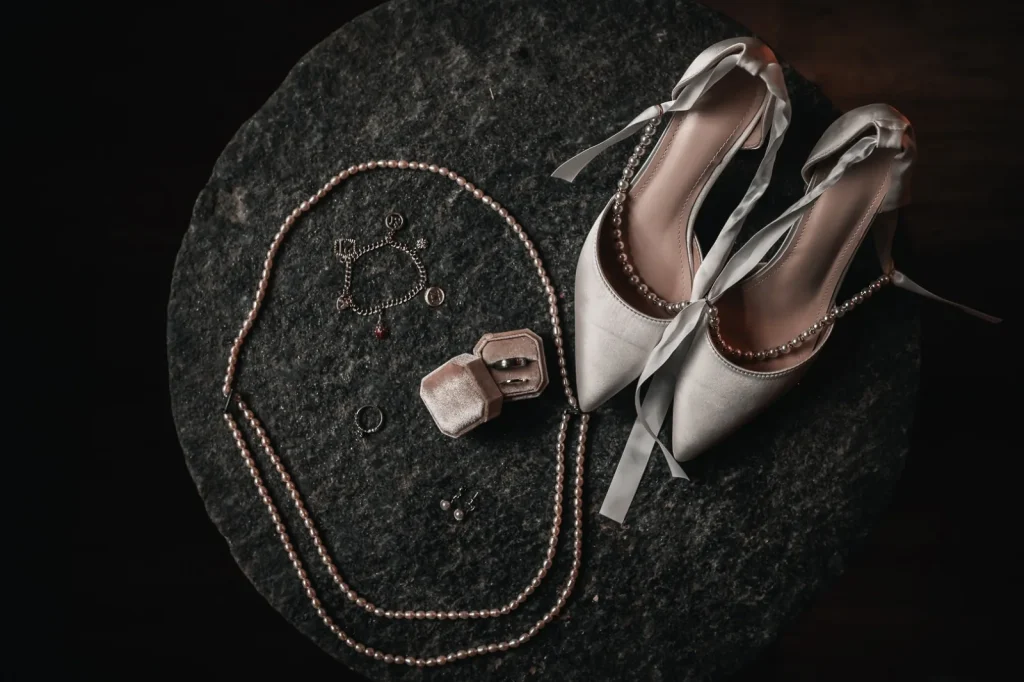Bridal shoes, a pearl necklace, a charm bracelet and rings in a velvet box laid out on dark slate