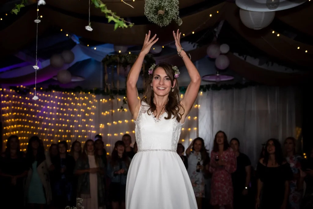 Bride throwing her bouquet on a fairy-lit dance floor as guests watch