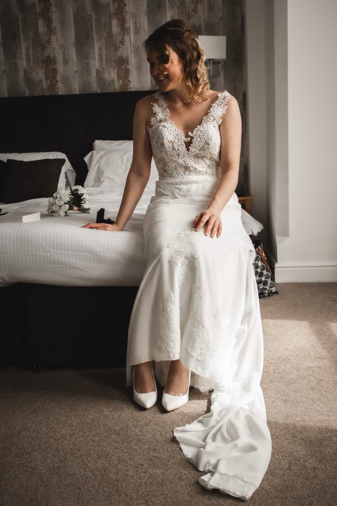 Bride sitting on the edge of a bed in her gown as she gets ready