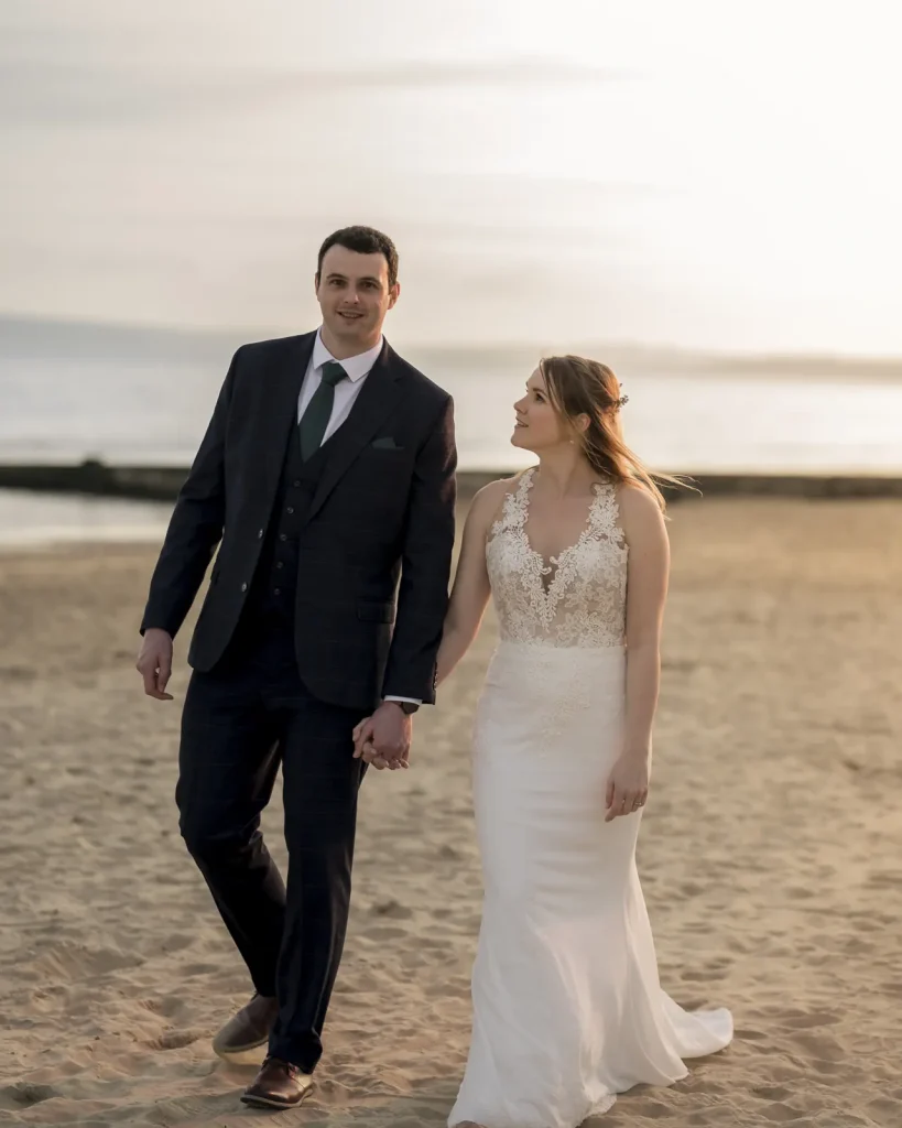 Bride and groom walking hand in hand along a beach at golden hour