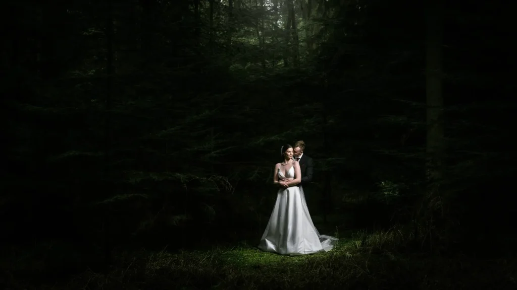Bride and groom embracing in a pool of light in a dark pine forest
