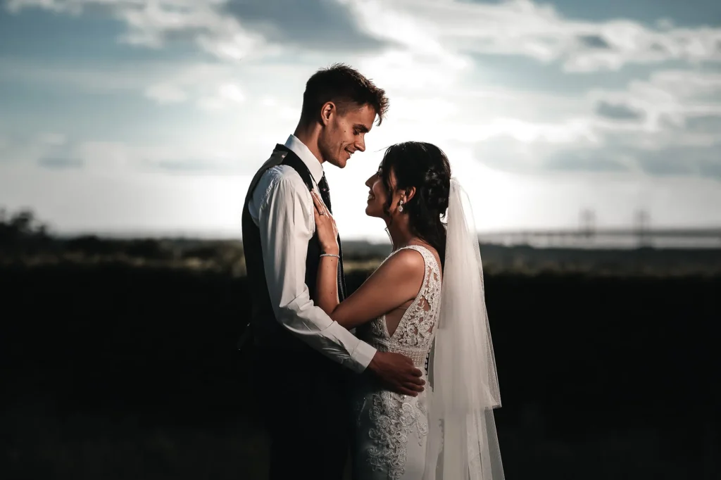 Bride and groom facing each other at sunset beneath a dramatic sky