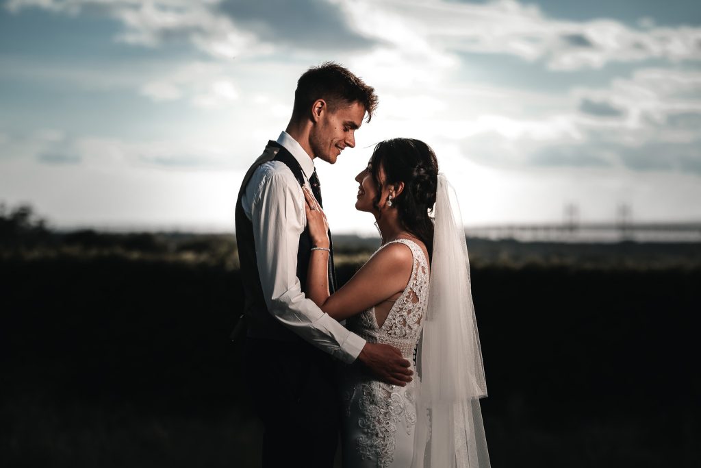 Bride and groom facing each other at sunset beneath a dramatic sky