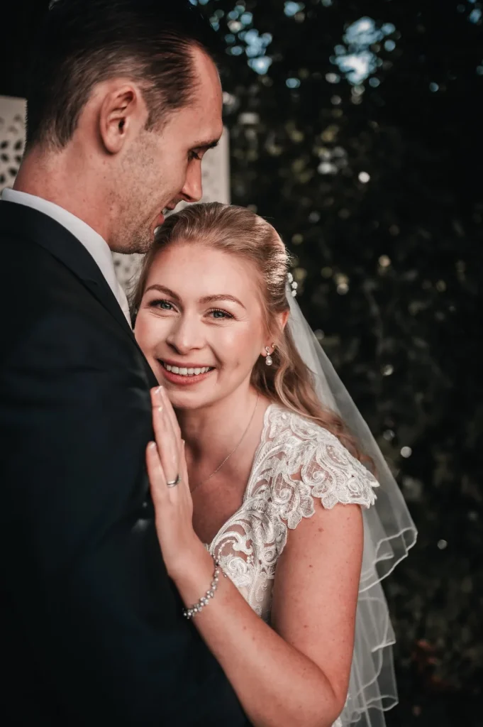 Bride smiling at the camera as she rests her head against the groom's chest