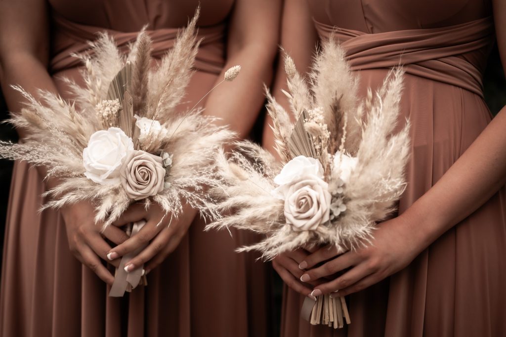 Bridesmaids in dusky pink dresses holding pampas grass and rose bouquets