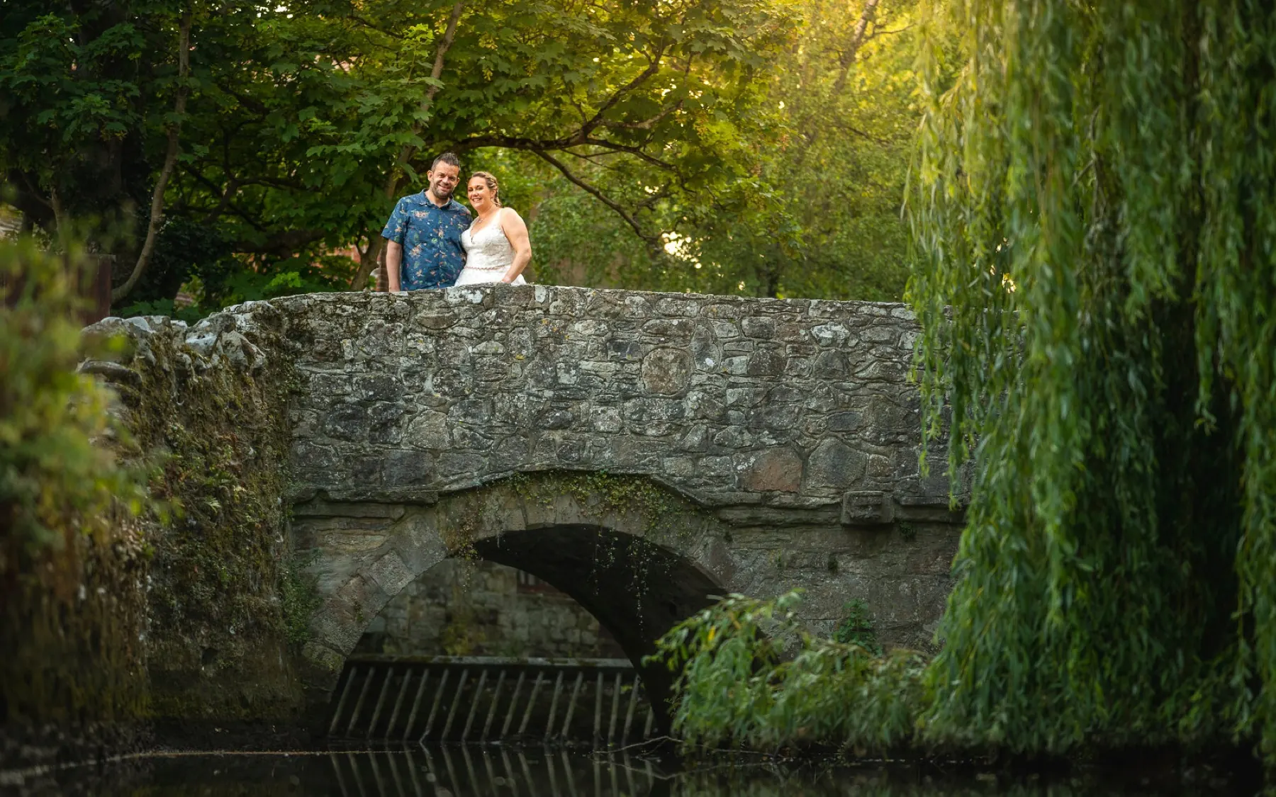 Couple standing on an old stone bridge framed by a weeping willow