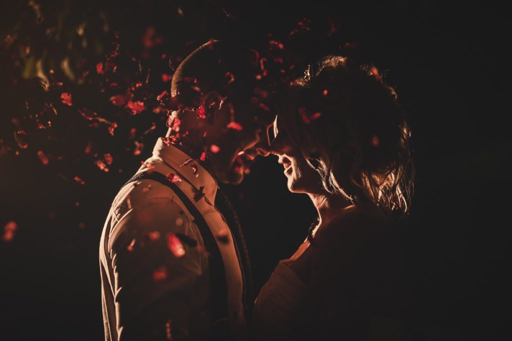 Close-up of a bride and groom touching foreheads in warm, dappled red light