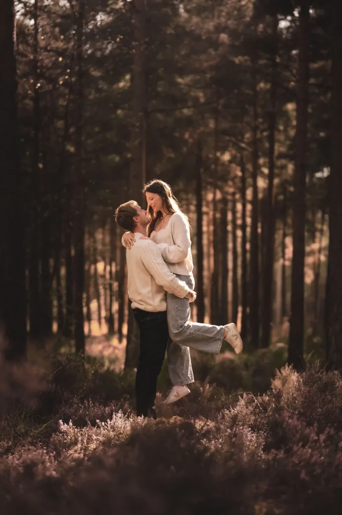 Man lifting his partner off the ground among pine trees and purple heather, the two smiling at each other