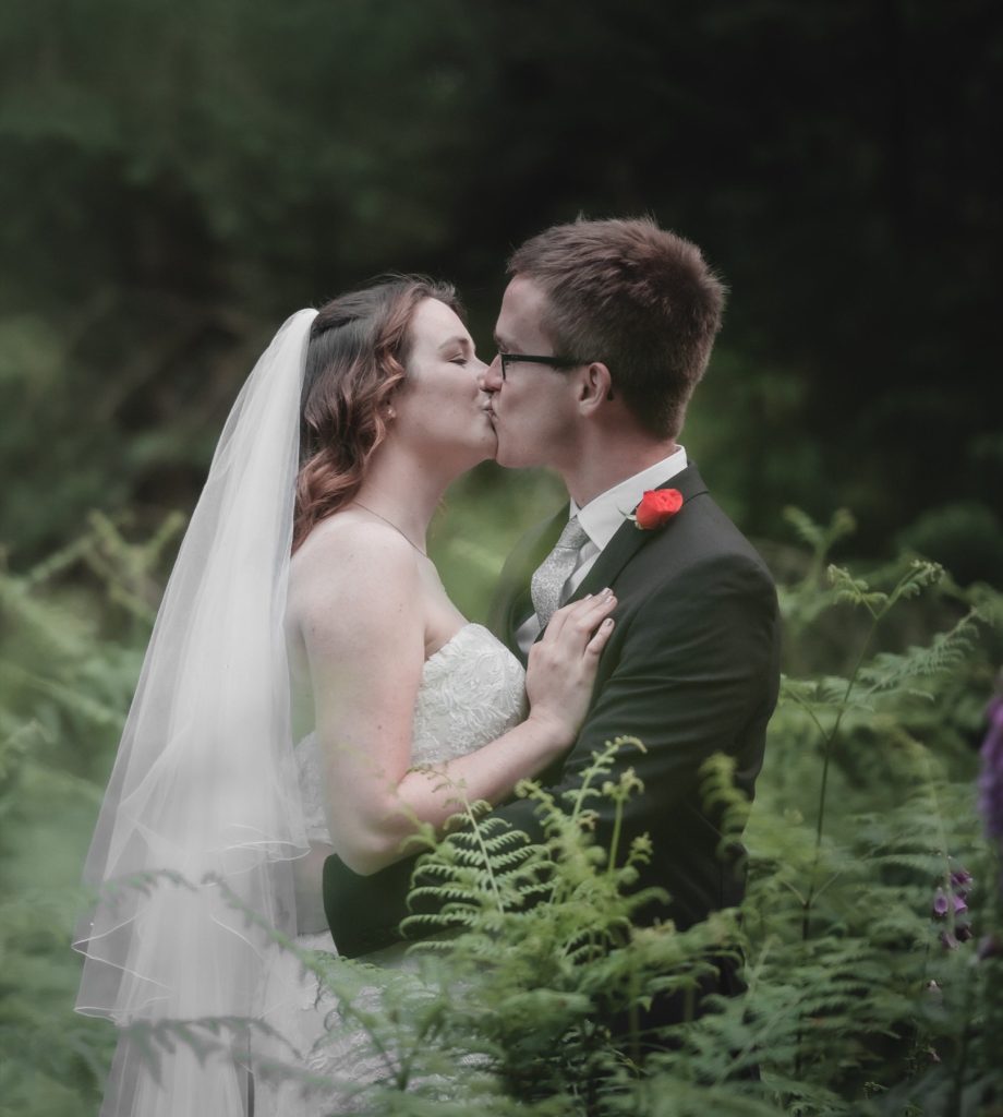 Bride and groom kissing among tall ferns