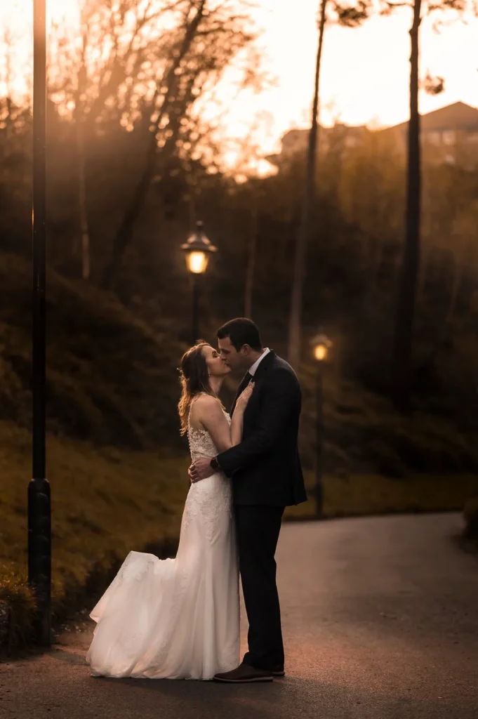 Bride and groom embracing on a lamplit path at dusk