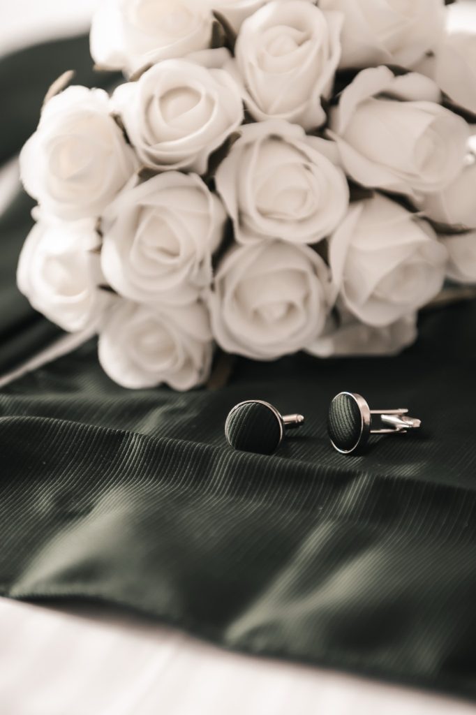White rose buttonholes and cufflinks laid on dark green fabric