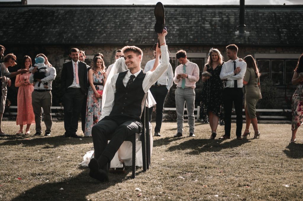Groom raising a shoe during the shoe game on the lawn as guests watch