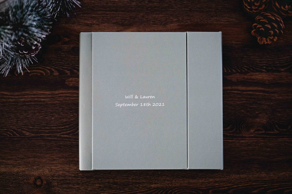 Linen-bound wedding album engraved with the couple’s names and wedding date, on a dark wooden table